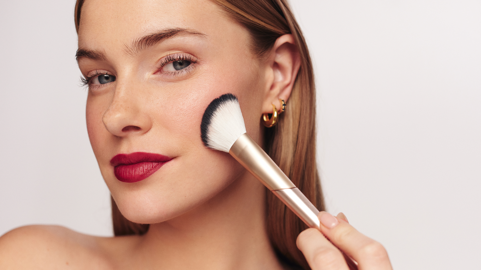 Model applying blush with Meroda Cosmetics makeup brush showcasing natural glow and premium beauty aesthetic